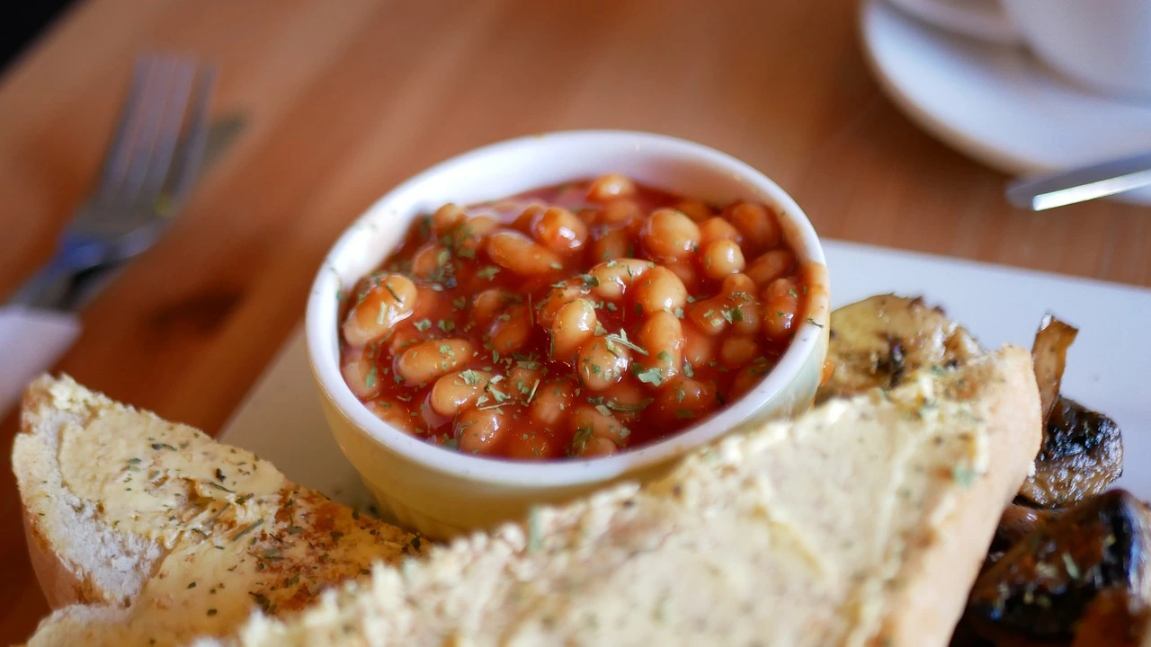 A bowl of baked beans garnished with herbs beside garlic bread and grilled vegetables.