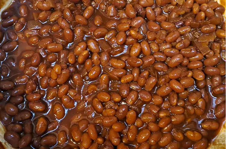 A bowl of homemade baked beans made from a canned baked beans recipe, garnished with fresh herbs on a rustic wooden table.