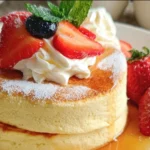 Fluffy Japanese soufflé pancakes stacked on a plate with syrup and berries