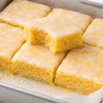 Fudgy lemon blondies stacked on a white plate with lemon slices