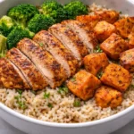 Healthy chicken and sweet potato rice bowl topped with fresh vegetables.