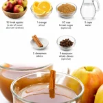 Glass of homemade apple cider surrounded by fresh apples and cinnamon sticks