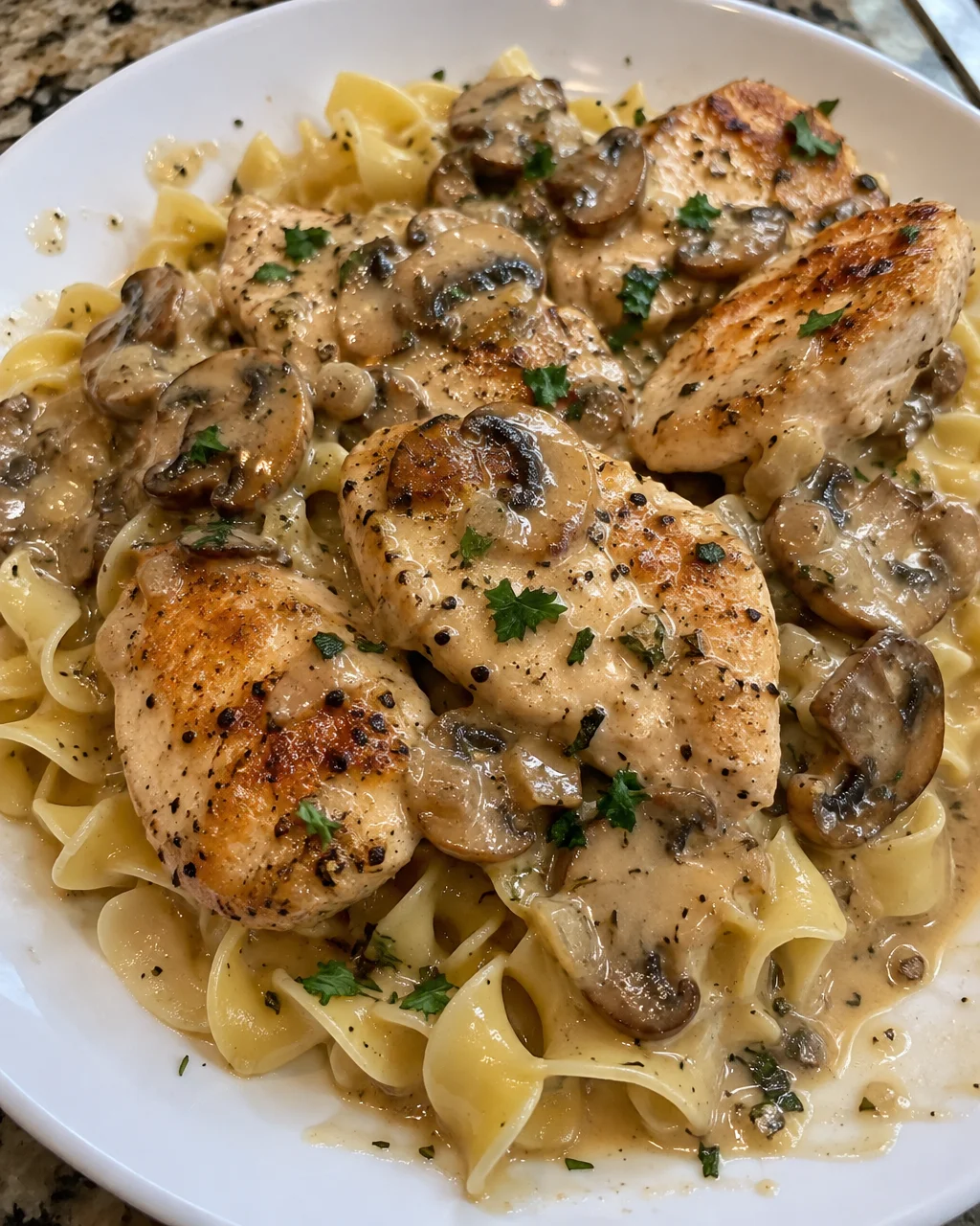 Creamy buttered noodles topped with grilled chicken on a white plate