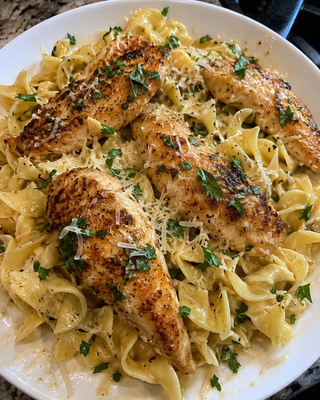 Plate of buttered noodles topped with garlic butter chicken, a delicious meal.