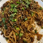 Plate of Mongolian ground beef with noodles garnished with green onions